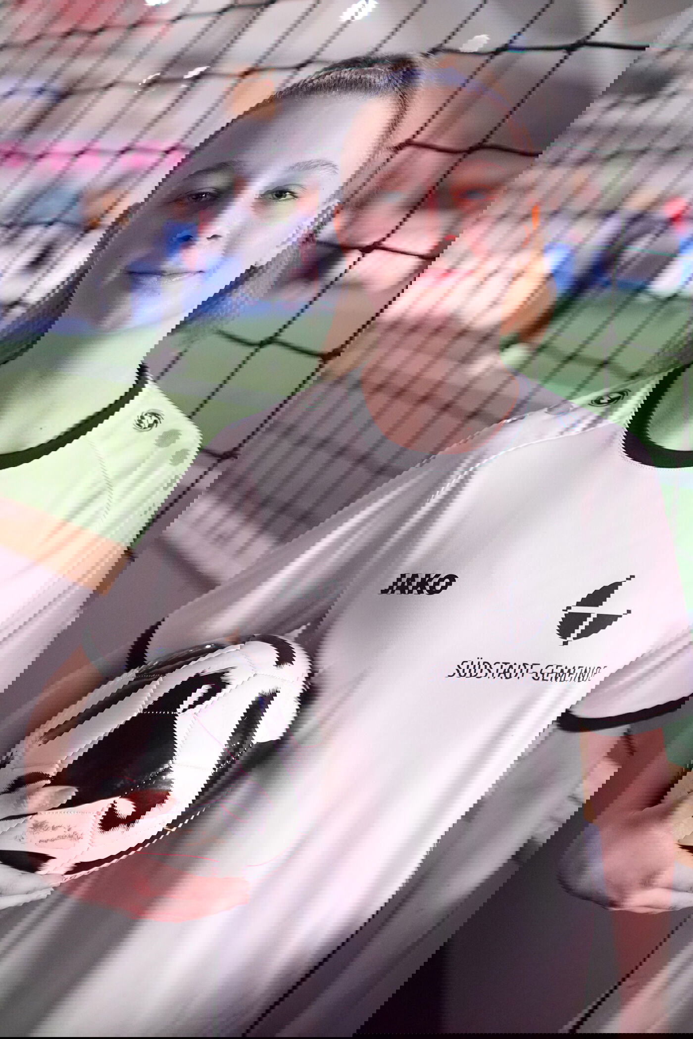 Ein Mädchen mit weißem Trikot und Fußball unter dem Arm.