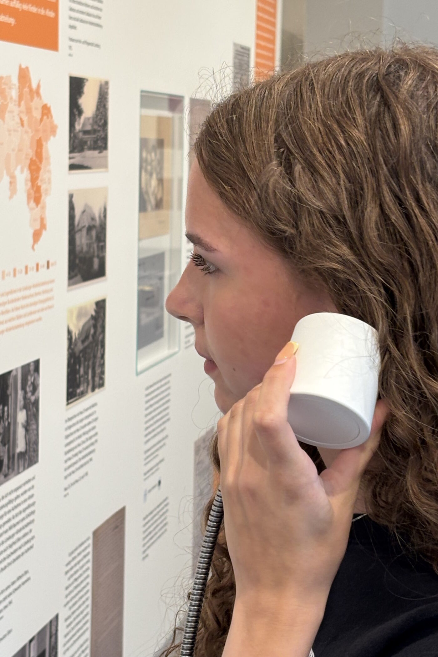 Ein Mädchen steht vor einer Ausstellungstafel und hält sich einen Kopfhörer ans Ohr.