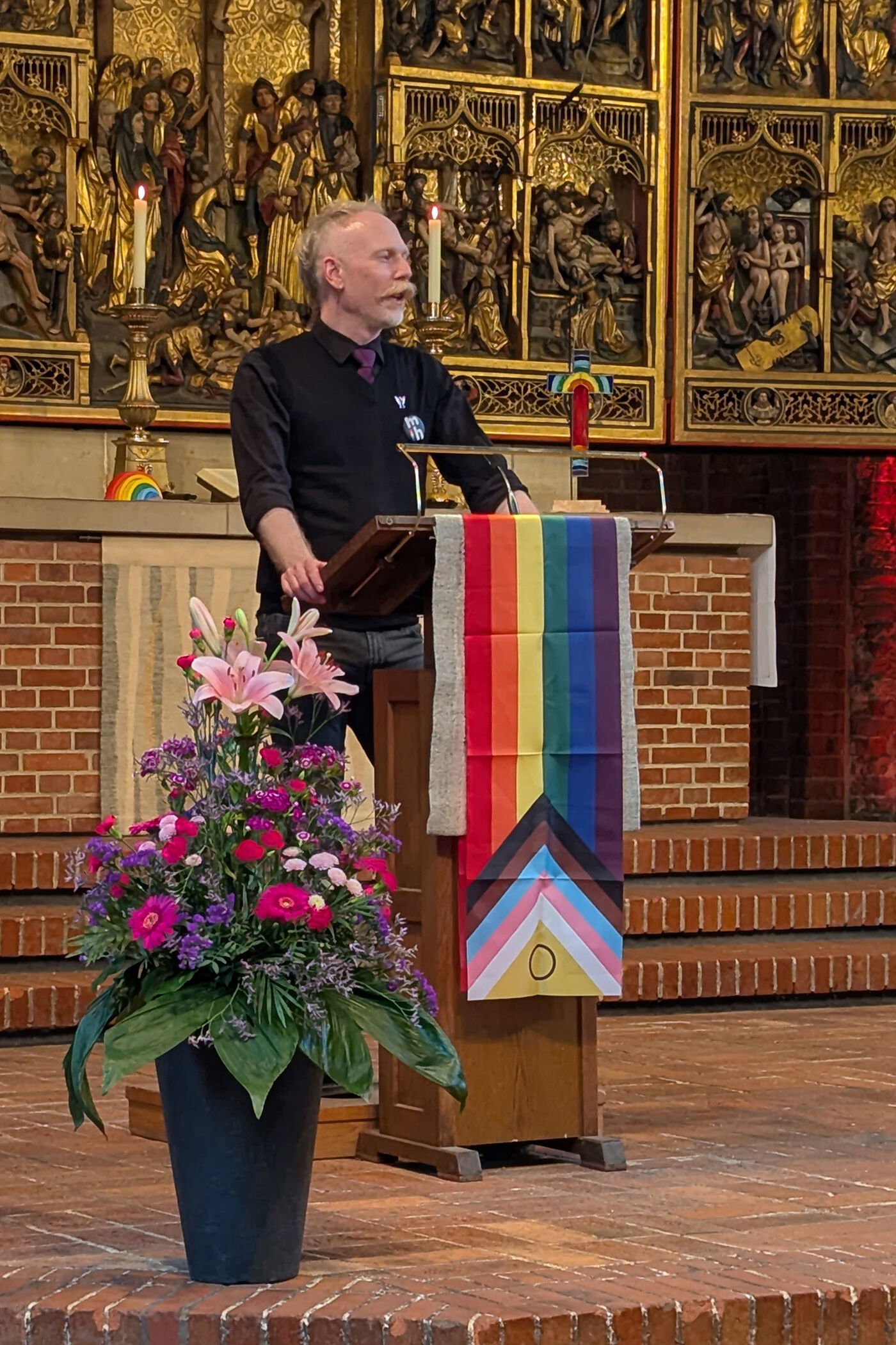 Eine als Mann lesbare Person an einem Redepult in einer Kirche.