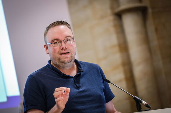 Eine männlich lesbare Person steht an einem Podium und spricht.
