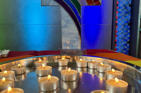 Teelichter auf einem Tablett dahinter ein Kreuz mit Regenbogen