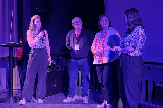 Vier Personen, männlich bzw. weiblich gelesen, stehen im Halbdunkel eines Kinosaals und führen mit Mikrophonen in der Hand ein Gespräch. 