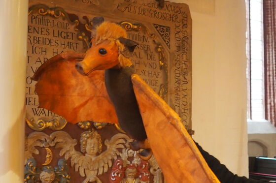 Eine Fledermaus-Handpuppe, bestehend aus einem Kopf mit großen Ohren und runder Nase und breiten braunen Flügeln.