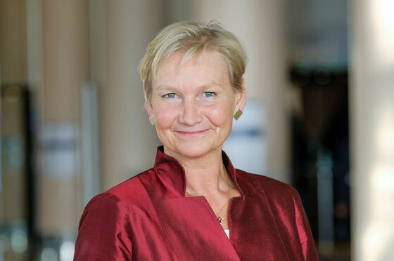 Eine weiblich gelesene Person mit kurzen, blonden Haaren und in satin-rotem Oberteil lächelt fröhlich. 