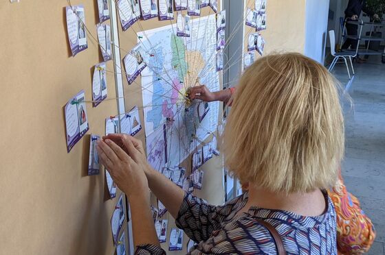 Eine Person mit kurzen blonden Haaren pinnt etwas an eine Stellwand, an der schon weitere Zettel hängen.