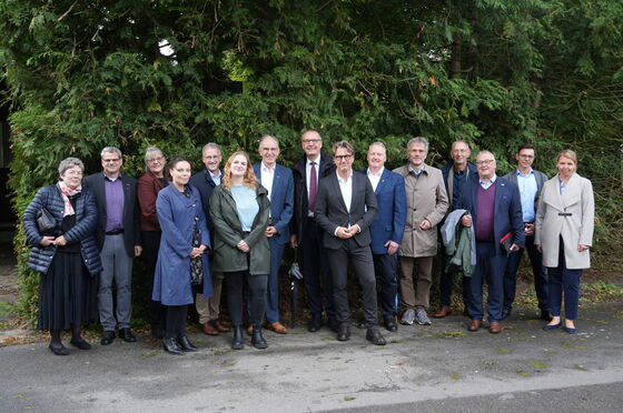 Eine große Gruppe posiert vor Nadelbäumen.