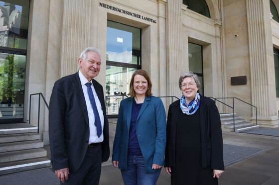 Eine als Mann und zwei als Frauen lesbare Personen vor einem alten Gebäude mit der Aufschrift Niedersächsischer Landtag.