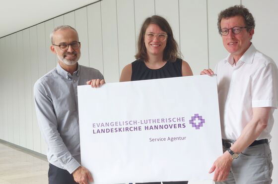 Zwei männlich zu lesende Personen und eine weiblich zu lesende Person halten ein Plakat.