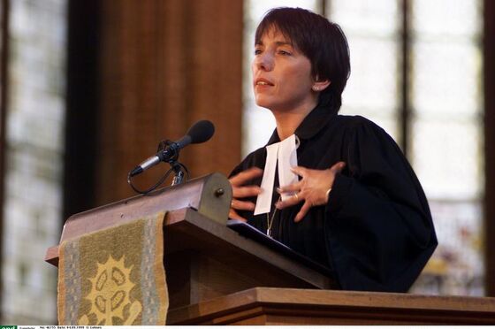 Eine weiblich zu lesende Person im Talar spricht auf einer Kanzel in ein Mikrofon.