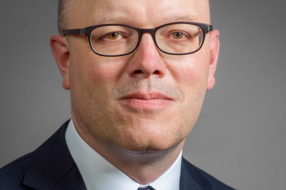 Portraitfoto einer männlich zu lesenden Person, die eine Brille, Krawatte und Anzug trägt.