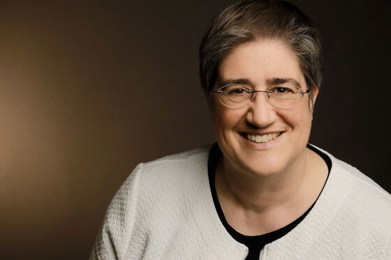 Ein weiblich zu lesende Person mit Brille lächelt.