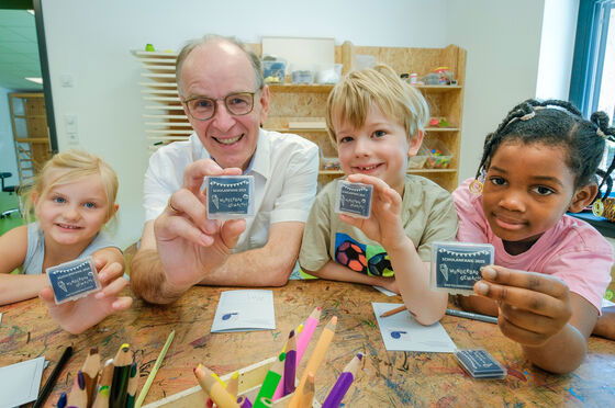 Eine als Mann lesbare mittelalte Person und drei Kinder halten einen kleinen Radierer in die Kamera.