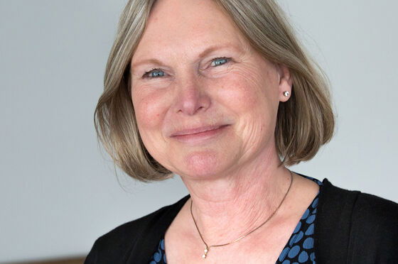 Eine blonde Frau lächelt vor einem grauen Hintergrund. 