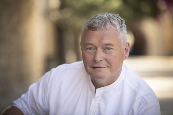 Ein Mann mit grauen Haaren und weißem Hemd, der Hintergrund ist verschwommen.