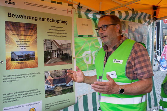 Eine männlich zu lesende Person, die eine grüne Weste trägt, spricht und gestikuliert.