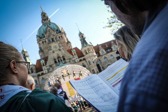 Blick über die Schulter eines Menschen, der in ein Liedblatt schaut. Im Hintergrund ist die Bühne vor dem Rathaus in Hannover zu sehen.