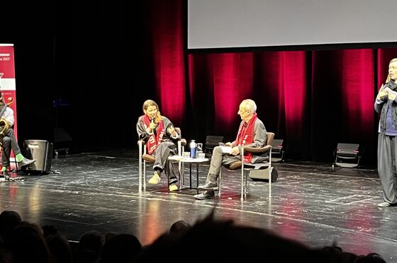 Eine weiblich und eine männlich zu lesende Person sitzen sich auf einer Bühne gegenüber und diskutieren miteinander.