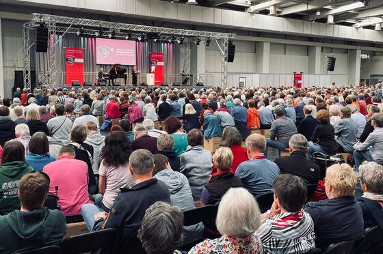 Blick aus dem Publikum in einer vollbesetzten Messehalle auf ein Podium