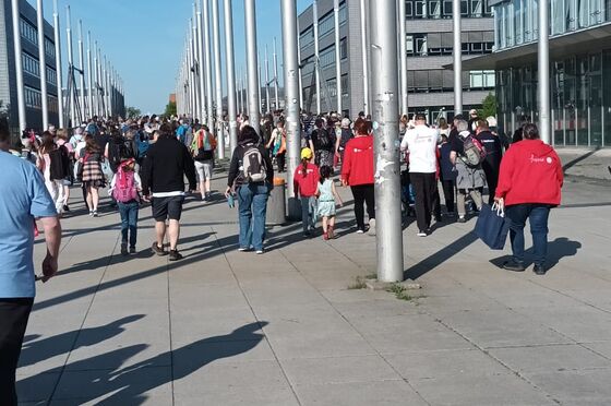 Blick aus der Perspektive einer Person im Rollstuhl auf einen asphaltierten Fußweg auf dem Menschen gehen.