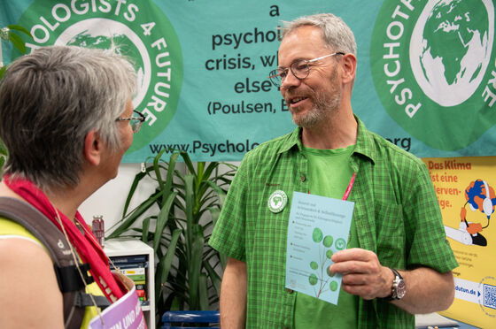 Eine männlich gelesene Person im Gespräch mit einer anderen. Im Hintergrund die Logos von Christians for Future und Psychologists for Future