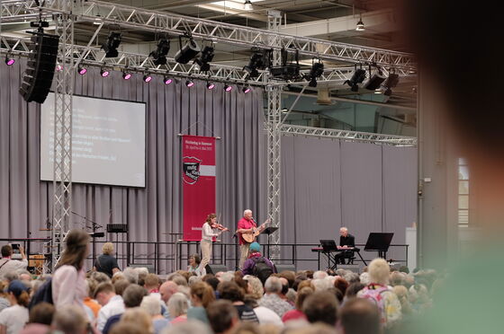 Eine männlich gelesene Person auf einer Bühne mit vielen Menschen davor.