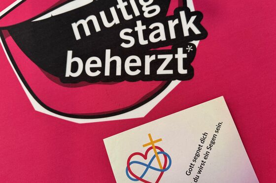Das Kirchentagslogo: ein Mund mit der Aufschrift mutig stark beherzt und eine Karte mit der Aufschrift: Gott segnet dich und du wirst ein Segen sein.