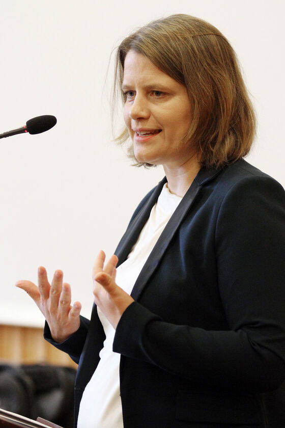 Eine jüngere Frau steht an einem Mikrofon und spricht.