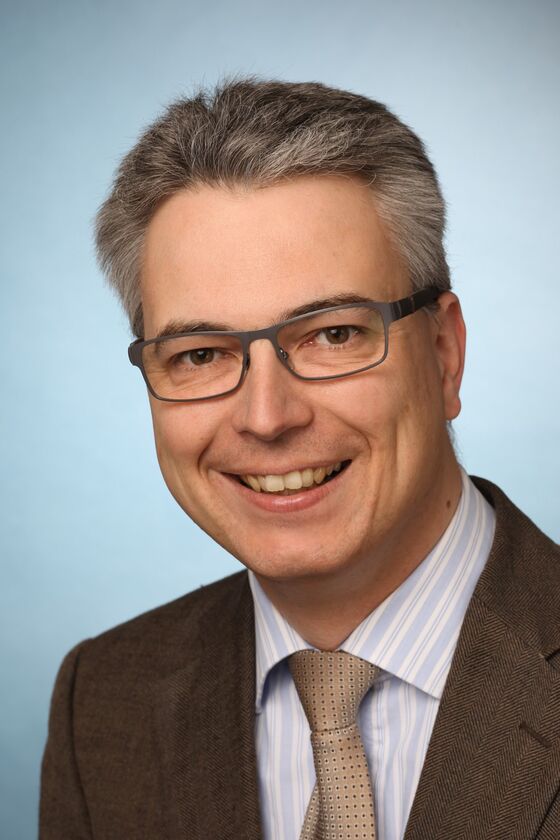 Ein Mann mit Brille im Anzug lächelt.