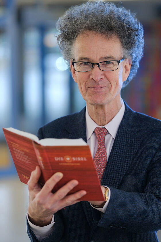 Eine als Mann lesbare Person mit Brille und im Anzug hält eine Bibel in der Hand.