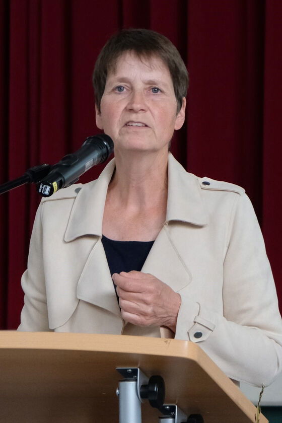 Eine als Frau lesbare Person steht an einem Redepult und spricht in ein Mikrofon.