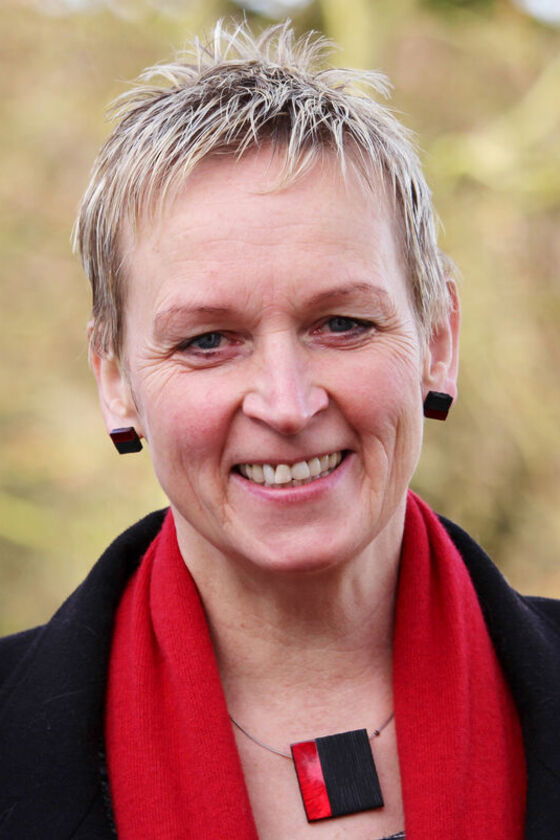 Eine als Frau lesbare Person mit Kurzhaarfrisur und rotem Schal.