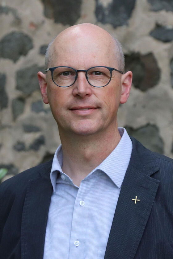 Eine als Mann lesbare Person mit Brille, Stirnglatze, hellblauem Hemd und dunkelblauem Sakko.