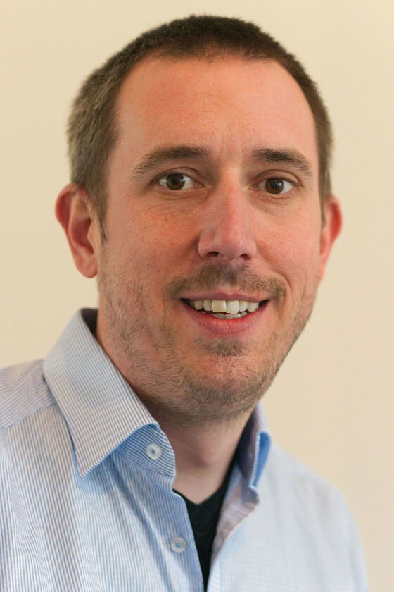 Eine männlich gelesene Person mit kurzen Haaren und hellblauem Hemd lächelt.