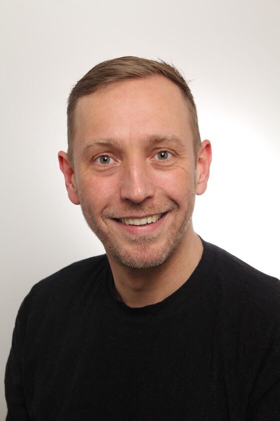 Ein junger Mann mit kurzen Haaren und schwarzem Pulli lächelt.