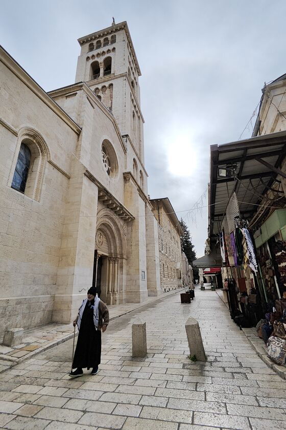 Ein Mann geht durch eine schmale Straße, die hell gepflastert ist, an einem Kirchturm vorbei.