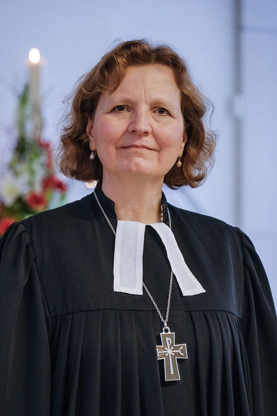 Eine Frau mit mittellangen Haaren, in Talar und einem Kreuz um den Hals blickt leicht lächelnd in die Kamera.