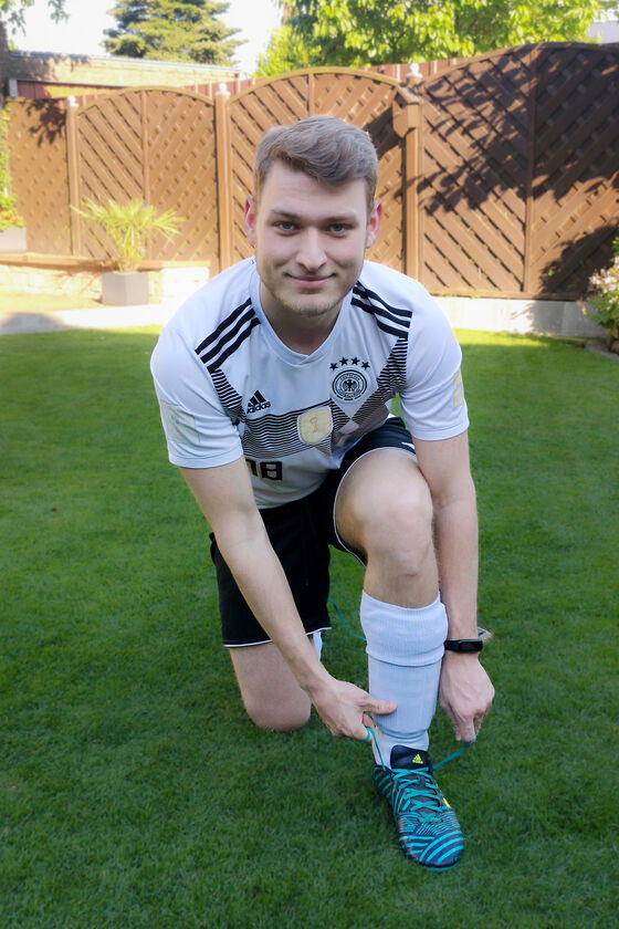 Eine als männlich gelesene Person im Fußball-Dress schnürt sich Fußballschuhe zu.