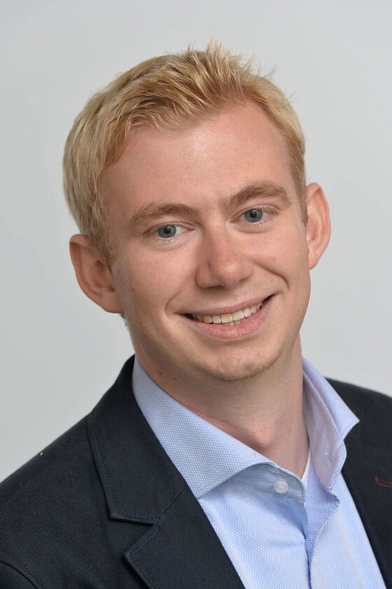 Eine männlich gelesene Person mit kurzen blonden Haare und blauem Hemd lächelt.