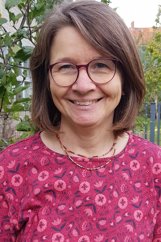 Eine weiblich gelesene Person mit kurzen Haaren, Brille und einem rotem Pullover.