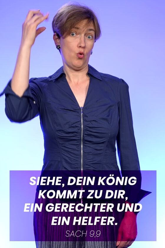 Eine weiblich gelesene Person in blauer Bluse gebärdet das Wort "König", mit der rechten Hand neben dem Kopf. Im unteren Bereich steht der Spruch: Siehe, dein König kommt zu dir, ein Gerechter und ein Helfer.