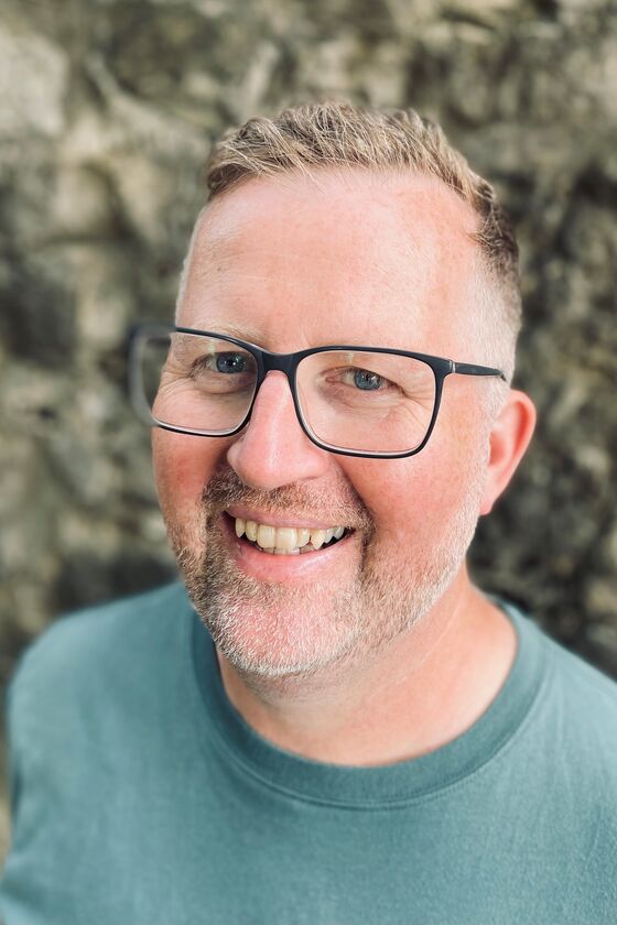 Eine männlich gelesene Person mit raspelkurzen Haaren und Brille lacht in die Kamera. Er trägt einen hellgrünen Pulli.