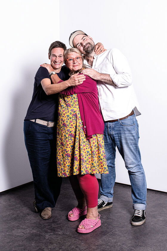 Drei Personen, zwei weiblich, eine männlich gelesen, umarmen sich eng.