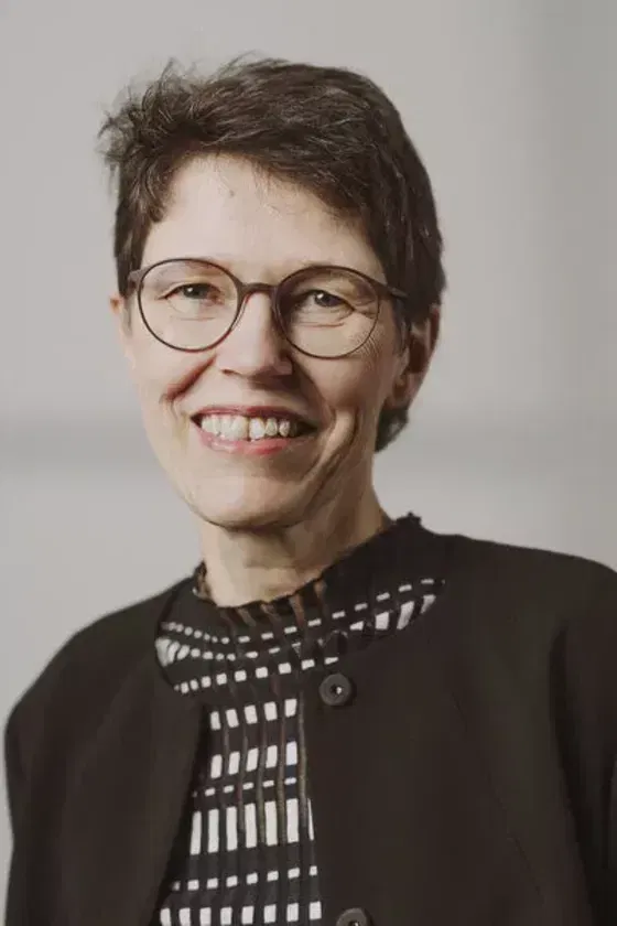 Eine weiblich gelesene Person mit dunklen kurzen Haaren und einer Brille mit dunkler Fassung. 