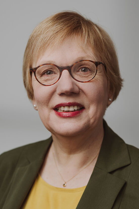 Portraitfoto einer als Frau lesbaren Person mit kurzen Haaren und Brille