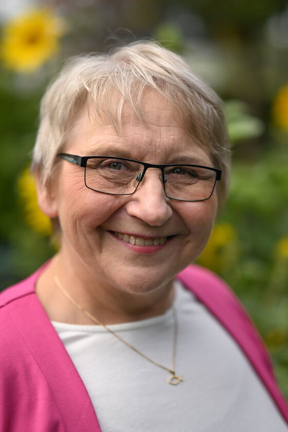 Eine weiblich gelesene Person mit Brille, weißem Shirt und rosa Jacke.