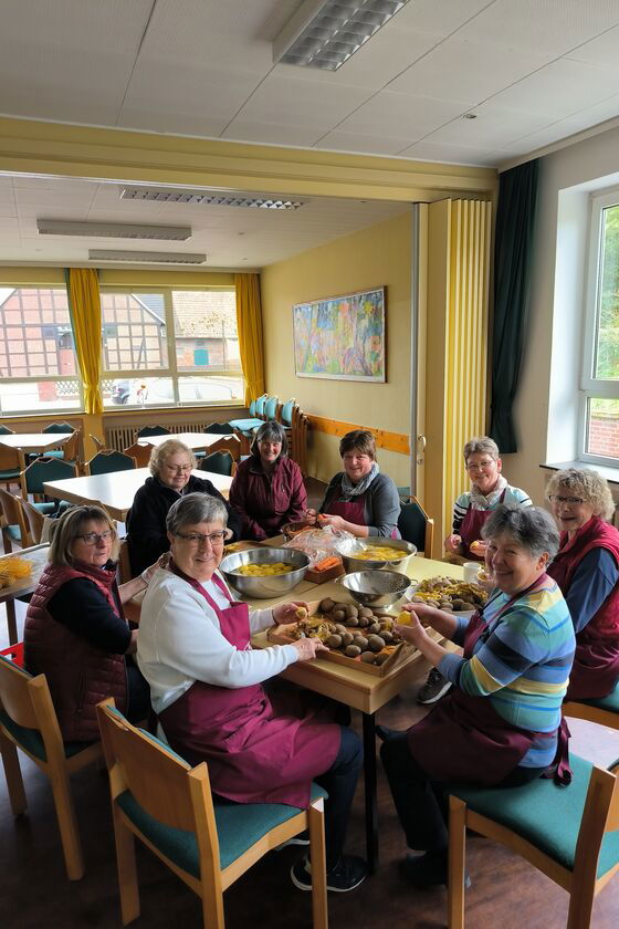Mehrere Personen sitzen an einem Tisch und schälen Kartoffeln.