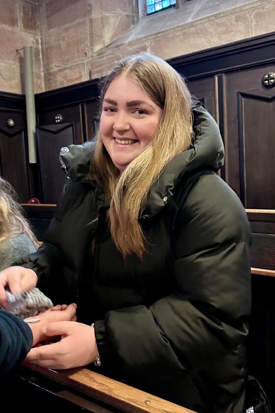 Eine junge, weiblich gelesene Person mit langen, blonden Haaren und schwarzer Jacke.