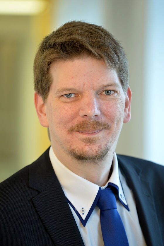 Eine als Mann lesbare Person im Anzug und mit Krawatte.