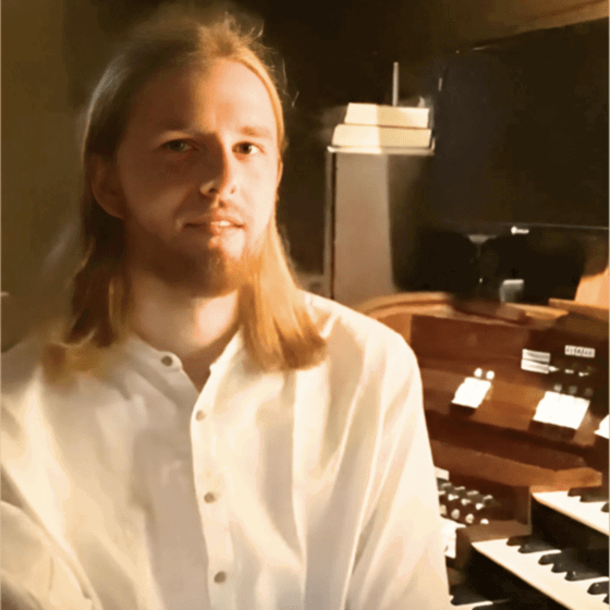 Ein Mann mit langen blonden Haaren sitzt vor einer Orgel.