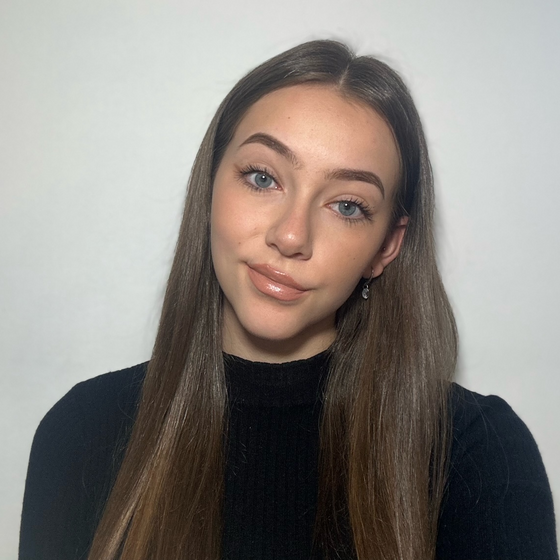 Eine junge frau mit langen, braunen Haaren und schwarzem Shirt neigt den Kopf nach rechts und schaut freundlich in die Kamera.